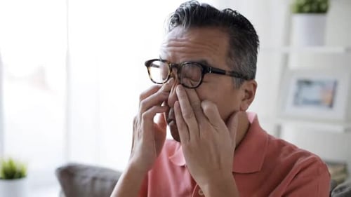 Concepto de visión, vista y personas: hombre cansado con gafas que se frota los ojos en casa en cámara lenta