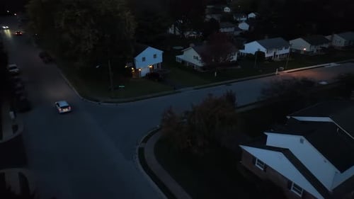 Car driving in American neighborhood at night. Aerial reveal of houses lining residential street wit