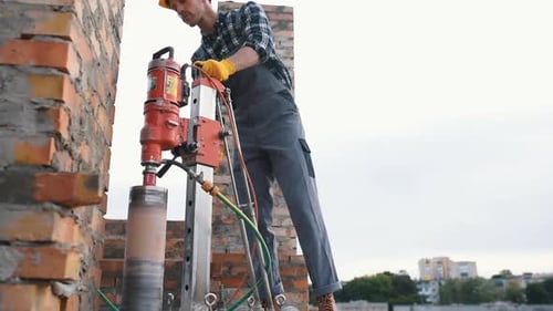 Uses electrical device. Construction worker in uniform and safety equipment have job on building