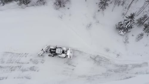 A Tractor Navigating a Snow-covered Country Road Bordered by Dense Coniferous Trees - Aerial Drone S