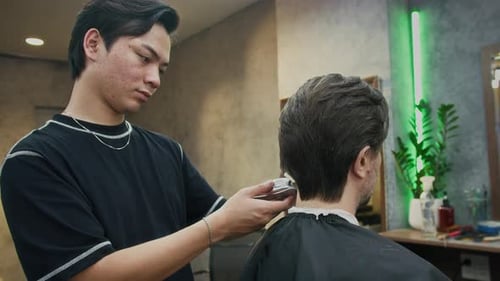 Serious Barber Trimming Hair of Male Client with Clipper