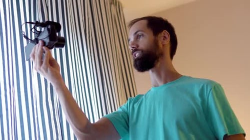 A Young Blogger Records a Video with Himself on His Camera in His Room Near Window