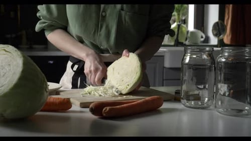 A housewife in an apron chops cabbage for fermentation at the kitchen table at home.