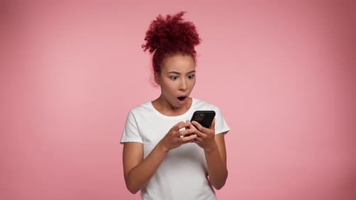 Mujer afroamericana pelirroja sorprendida que usa un teléfono inteligente navegando mira cámara