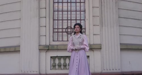 An Elegant Woman in a Vintage Dress Stands By an Old Stone Column