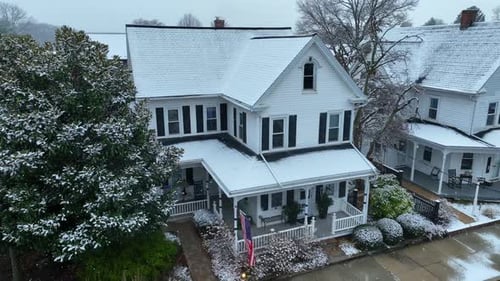 Snow covered town home in USA town with American flag on porch. Aerial descending shot during snow f