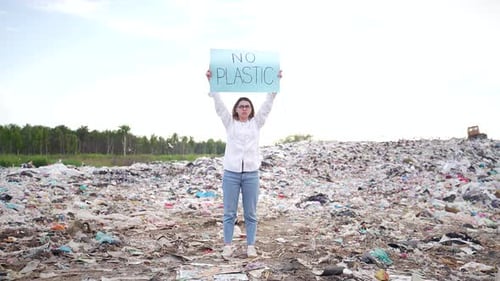 Ecology activist holding No Plastic poster. woman or girl standing by among a large landfill. Female