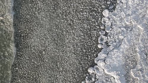 A frozen lake with intricate ice patterns and clear water at the edge, aerial view