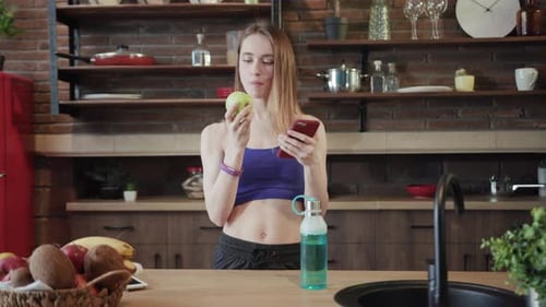 Healthy Lifestyle A Woman Holding an Apple and Using a Phone in a Modern Kitchen Setting