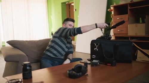 Man in Striped Sweater Reaching for Camera Equipment Bag Surrounded By Camera