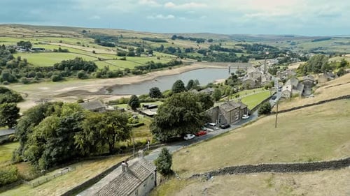 Aerial footage of a rural industrial village with old mill and chimney stack surrounded by fields an