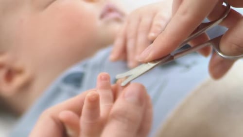 Caring Mom Cutting Baby Nails on Tiny Baby's Fingers