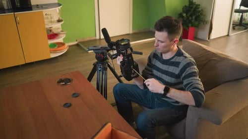 Studio Guy Adjusting Camera Lens and Preparing Gear for Video Shoot in Home Studio