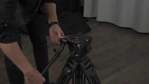 A Cameraman Opens and Sets a Tripod for a Professional Camera in a Studio Detail of the Shooting