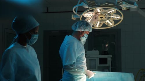 Male Surgeon in Sterile Gloves Surgical Uniforms and Masks Adjusting Light Before Operation in