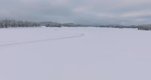Aerial view flying towards yellow rally car drifting corners on Swedish Lapland wintry woodland ice
