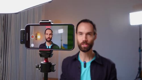 A Young Bloger Records a Video with Himself on Smartphone in His Room Studio