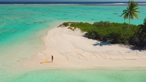 Mulher andando em uma praia tropical com viagem escrita na areia