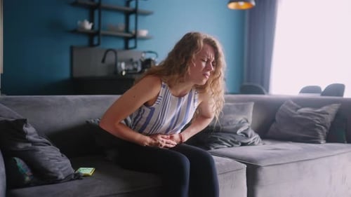 Caucasian Woman Suffering From Severe Stomach Ache Sitting on Sofa in Living Room Feeling Extremely