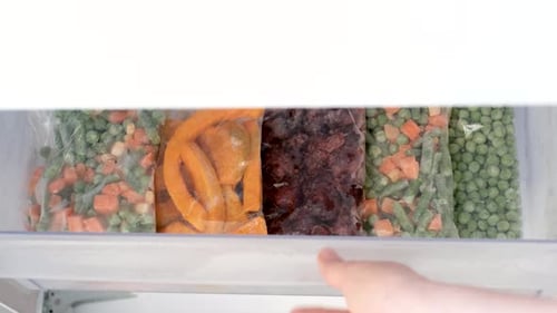 Cellophane bags with colorful frozen vegetables in freezer drawer top view.