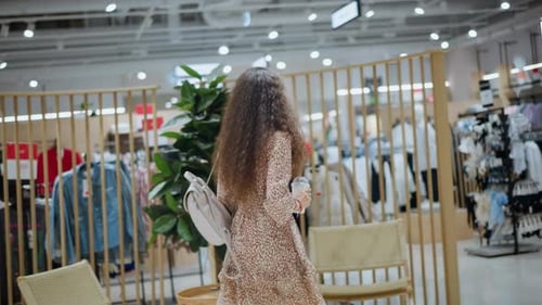 Woman Browsing Clothing Store with Backpack Surrounded By Trendy Apparel