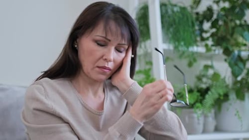 Mujer madura triste sentada en el sofá de su casa con problemas de salud