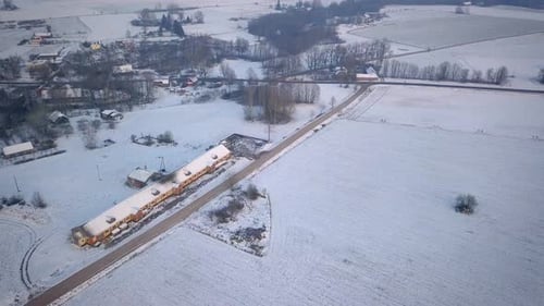 House Roof Covered With Snow And Bare Trees On Winter Field In Latvia - aerial descending forward