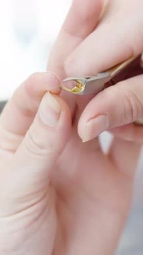 A woman bites off the skin from her finger with manicure tweezers, close-up. Vertical video.