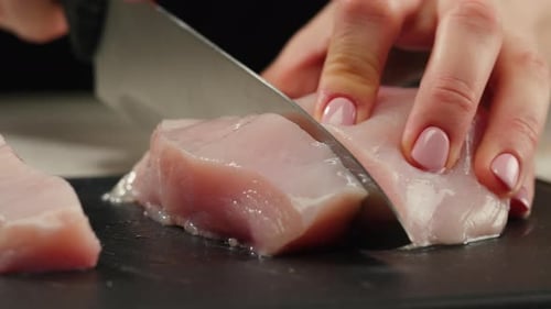 Man Slicing Raw Turkey or Chicken Meat Fillet on Oak Cutting Board Closeup Cooking with Knife on