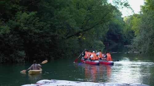 A Group of People Wearing Protective Helmets and Life Jackets are Rafting on a Peaceful River