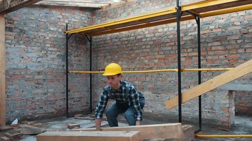 Walks with piece of board. Construction worker in uniform and safety equipment have job on building