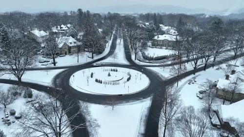 Aerial flyover of a traffic circle roundabout. Vehicles driving in snowy landscape. Large homes in U