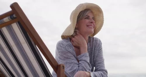 Thinking, old woman and relax on holiday in summer with chair at the beach in retirement