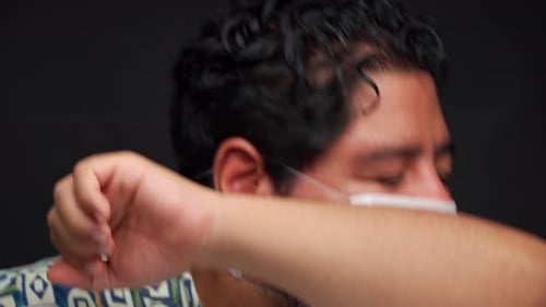 Hombre latino estornuda con tapabocas