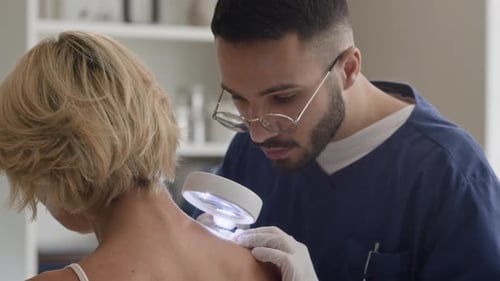 Focused Male Dermatologist Examining Skin on Shoulders through Magnifying Glass
