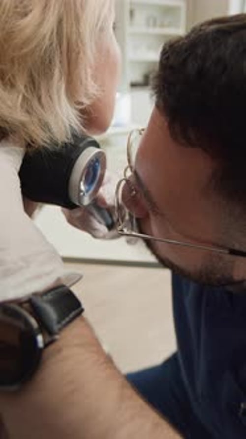 Male Dermatologist Examining Neck of Female Patient with Dermatoscope