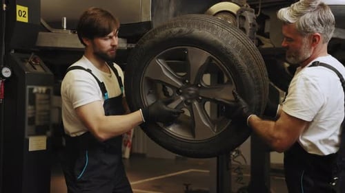 Two Caucasian Male Mechanics Checking the Condition of Tires of a Car Sent to a