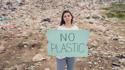Ecology activist holding No Plastic poster. woman or girl standing by among a large landfill. Female