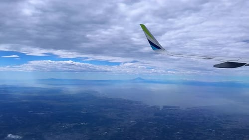 View of airplane wing flying over vast landscape with mountains and cloudy sky
