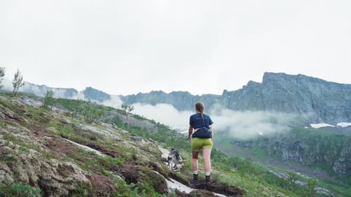 Couple Hiking With Their Pet Dog Overlooking The Rocky Mountain Covered by Clouds. - wide