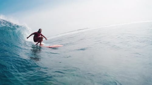 Surfer in red wetsuit rides the ocean wave on the longboard in tropical Maldives