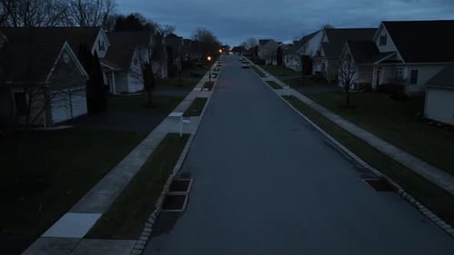 Aerial view of a symmetrical American suburb at twilight, with streetlights on, showcasing identical