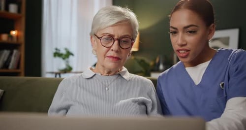 Senior woman, caregiver and laptop in home for help, support and care on sofa in living room