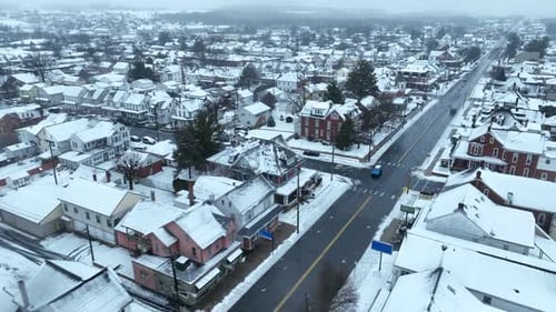 Snow-covered town with rows of houses and a main road. Aerial view during winter snow snowfall.