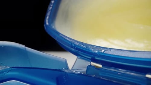 With my finger I take vaseline from a blue jar, on a black background. Dolly slider extreme close-up