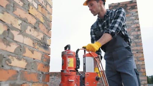 Uses electrical device. Construction worker in uniform and safety equipment have job on building