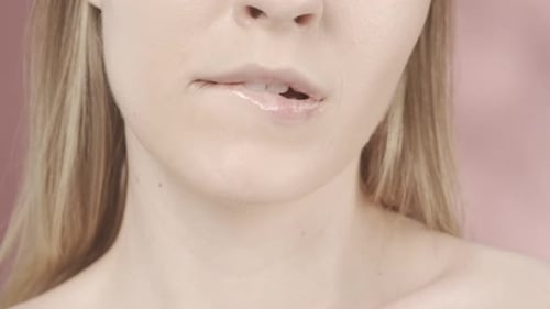 Une femme semi-nue s'est mordu la lèvre inférieure dans un studio sur fond rose. Les lèvres séduisantes d'une femme avec un