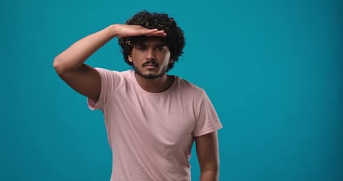 Joven indio busca a alguien y luego agita la palma de la mano en gesto de saludo da la bienvenida a alguien