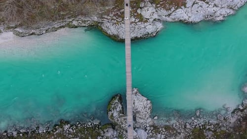 People walking on a suspension bridge over the emerald Soca River in Slovenia