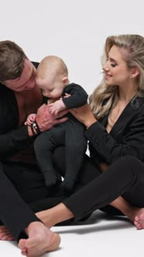 Caucasian couple in black suits sit on the floor with their infant son.